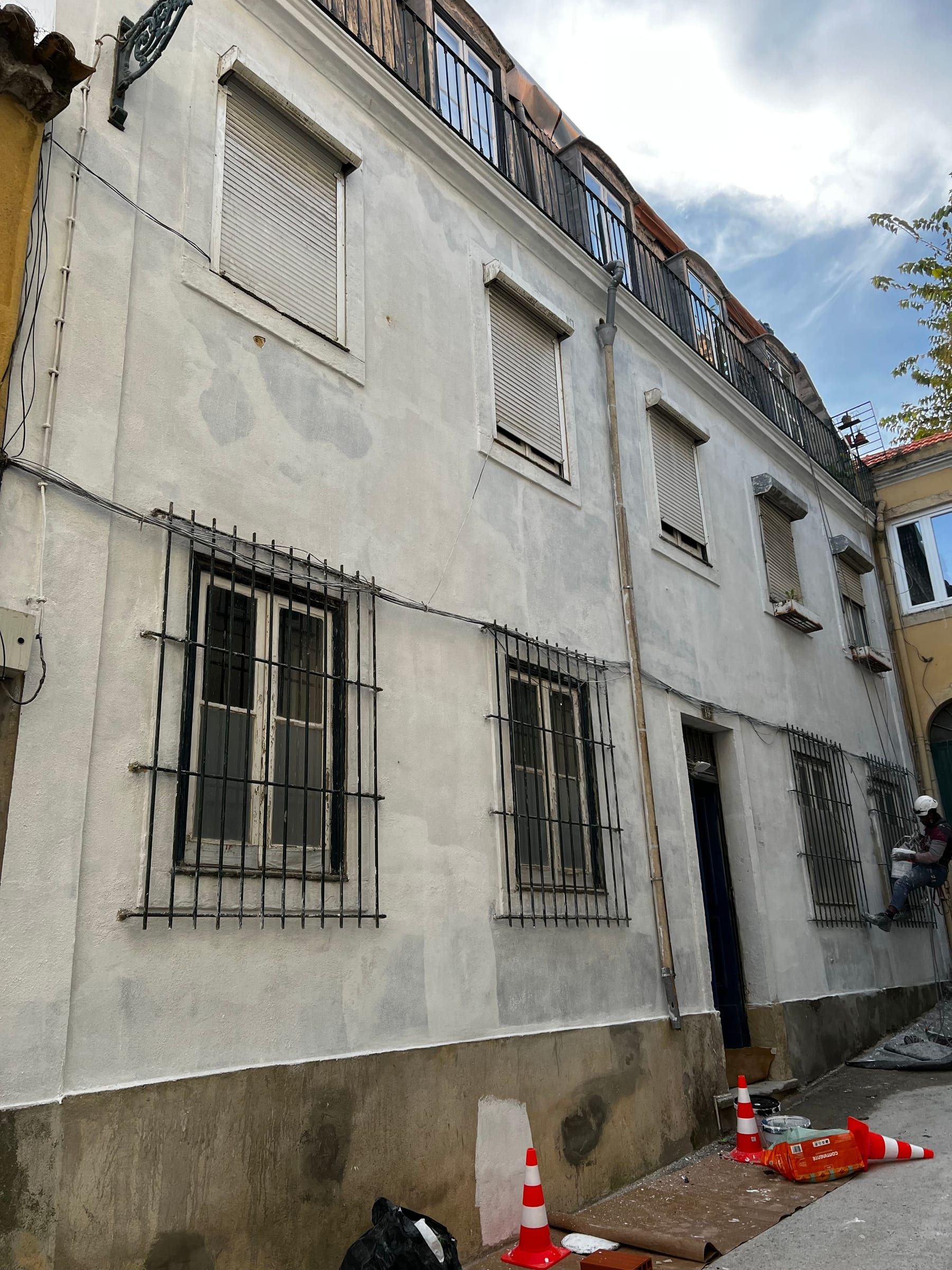 Fachada de edifício antigo em reparação, com um técnico suspenso por cordas