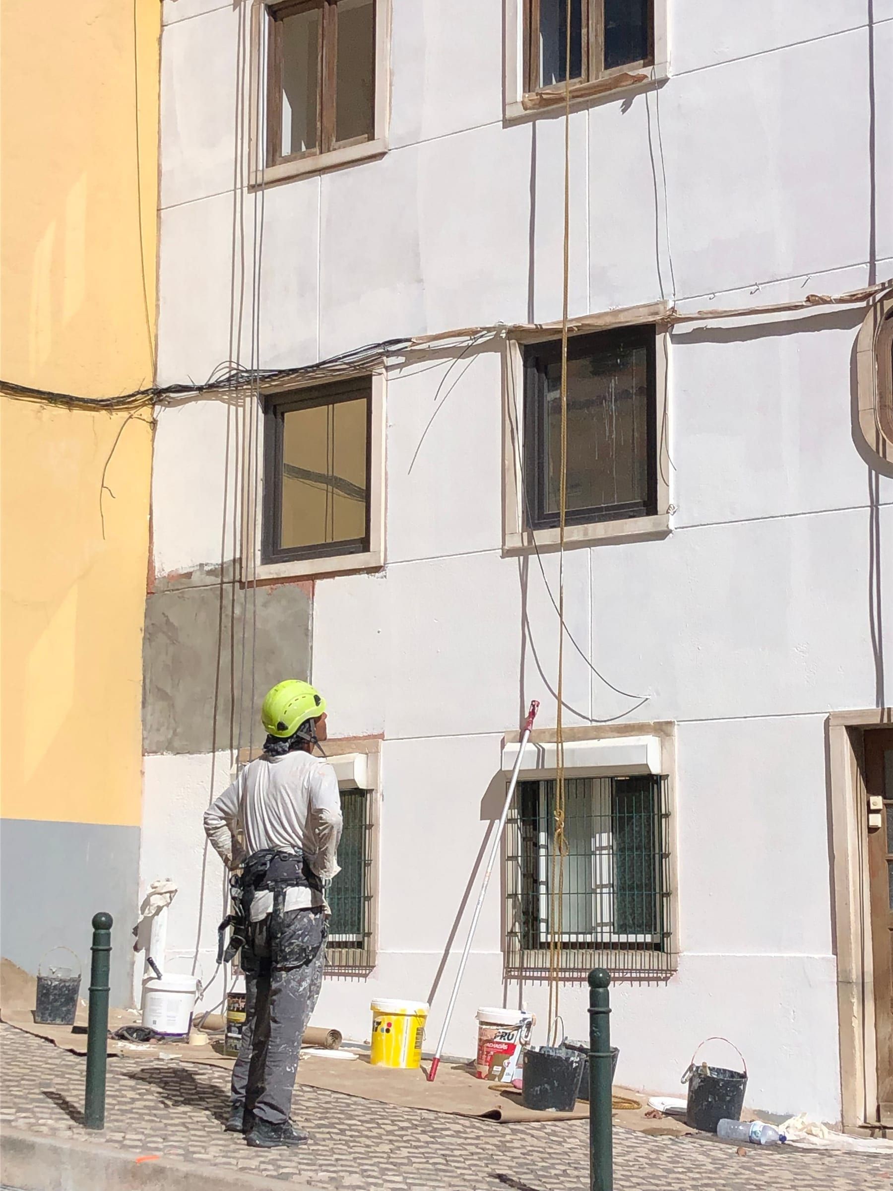 Técnico com capacete e arnês junto a uma fachada, com cordas de acesso suspensas