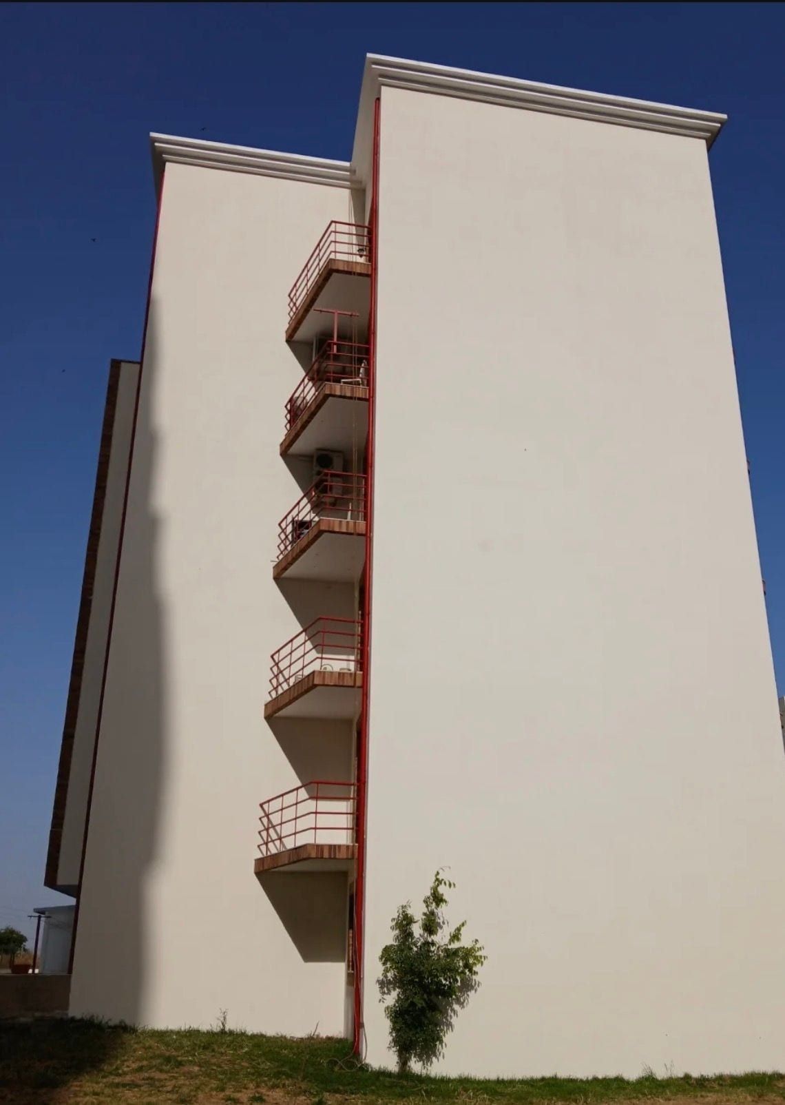 Fachada lateral de prédio pintada em branco, com varandas de guardas vermelhas
